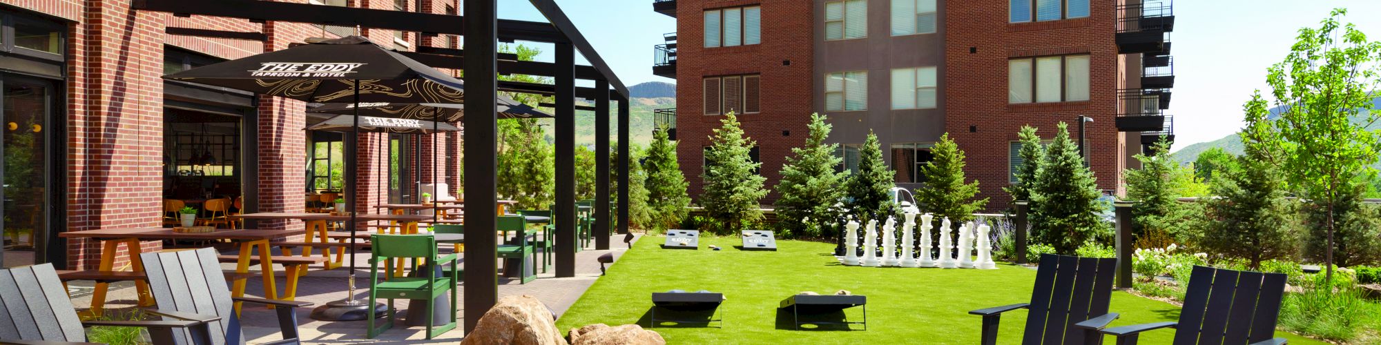 The image shows an outdoor communal area with chairs around a fire pit, a pergola, and a lawn with a large chess set. End of sentence.