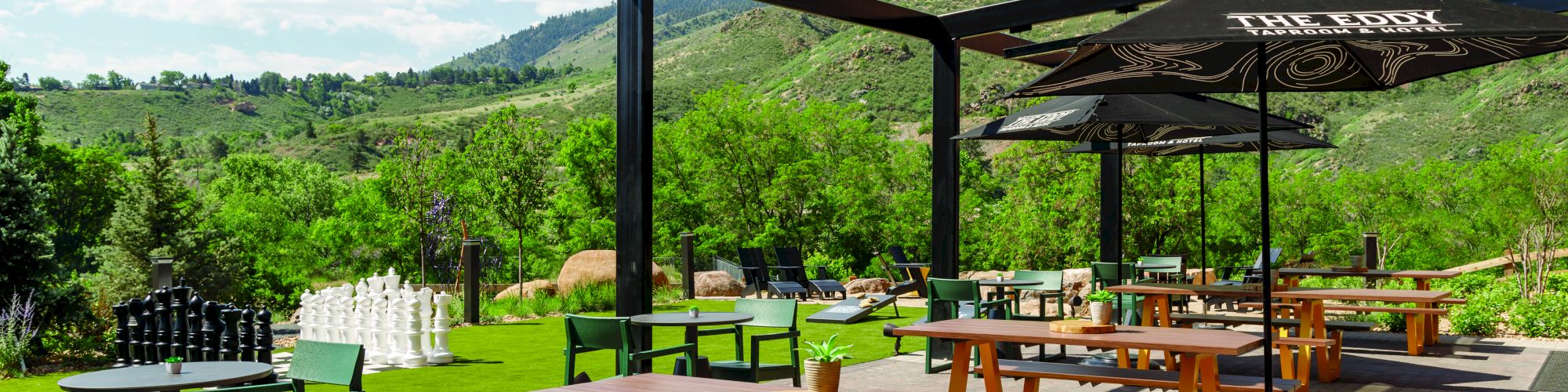 An outdoor patio with picnic tables, chairs, umbrellas, and a scenic view of green hills and clear skies, providing a peaceful dining atmosphere.