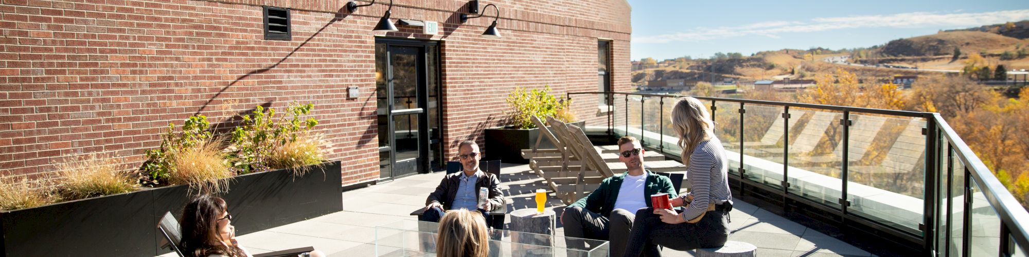 A group of people relaxing on a rooftop patio at "The Eddy Taproom & Hotel" with a scenic view of the landscape in the background.