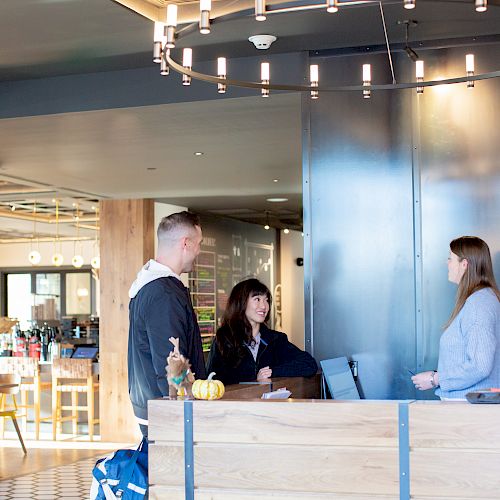 Three people are engaging at a reception desk in a modern, well-lit interior with wooden elements and a chandelier overhead ending the sentence.