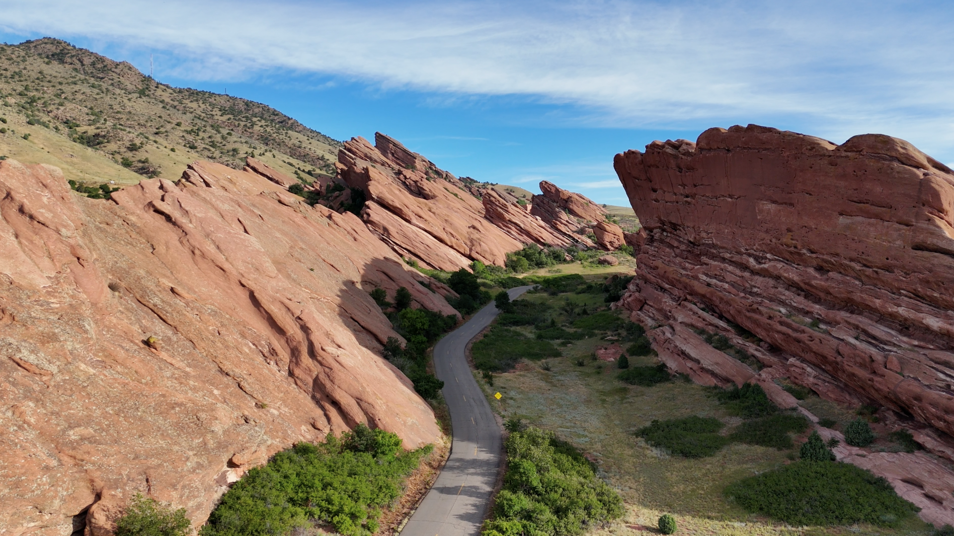 A scenic view of a road between large red rock formations under a blue sky, surrounded by green vegetation.
