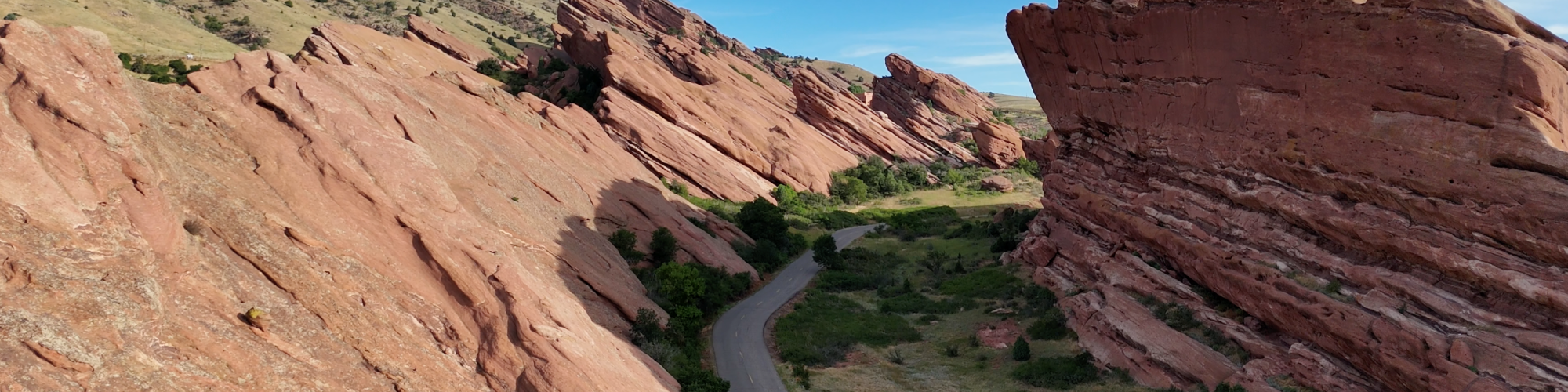 A scenic view of a road between large red rock formations under a blue sky, surrounded by green vegetation.