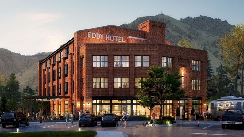 This image shows a brick building labeled "Eddy Hotel" set against a mountainous backdrop, with people and cars in the foreground.