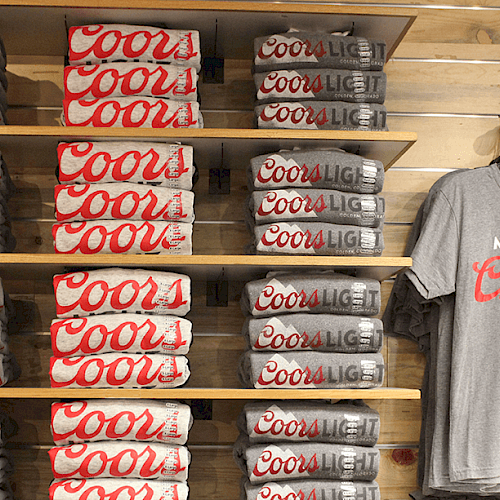 Stacks of folded Coors Light T-shirts on shelves with one gray T-shirt that reads "MADE TO Chill" hanging on the right.