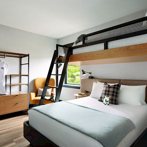 A modern hotel room with a bunk bed setup, cozy double bed, wooden furniture, and white robes hanging on a rack.