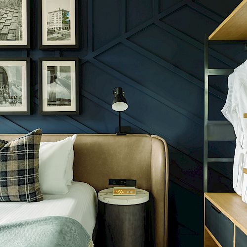 A cozy bedroom with a plaid pillow, wall art, a side table with a lamp, and a robe hanging on a shelf unit.