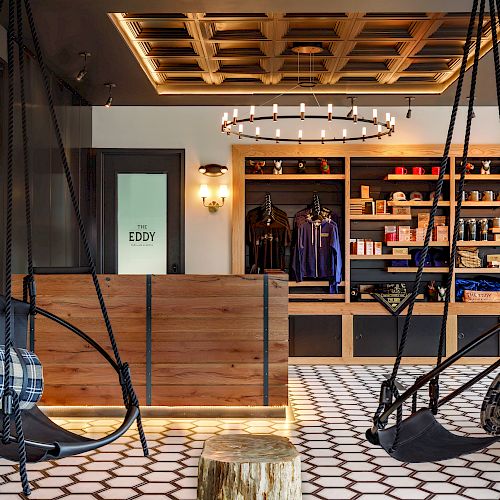 The image shows a modern lobby with hanging chairs, a wooden counter, shelves with various items, and a geometric floor pattern.