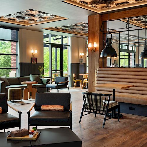 This image shows a modern cafe or lounge area with large windows, comfortable seating, wooden accents, and pendant lights hanging from the ceiling.
