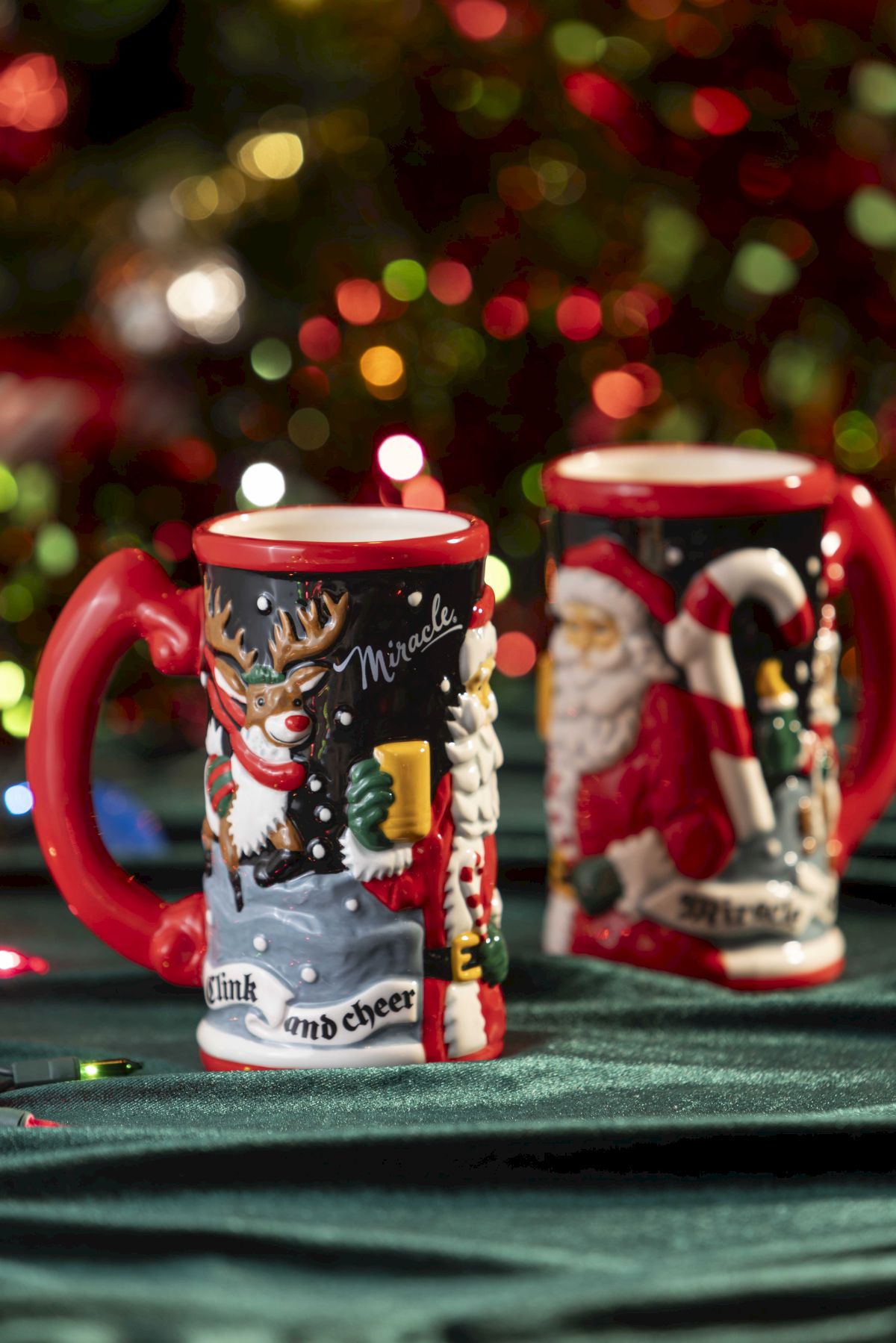 Two festive holiday mugs&mdash;one with a reindeer &ldquo;Miracle,&rdquo; the other Santa&mdash;against a colorful bokeh Christmas light backdrop.