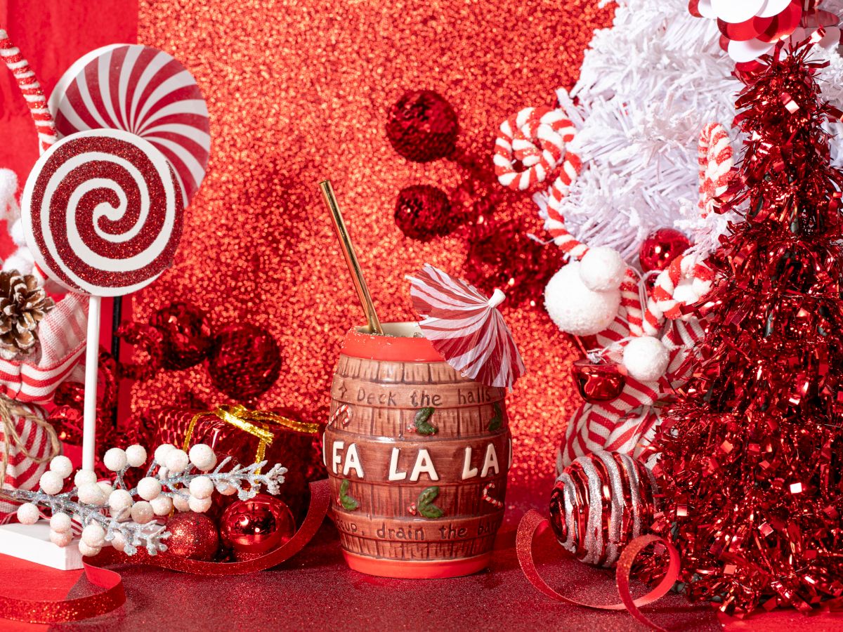 Festive scene with red and white decorations, candy canes, lollipops, a red tree, and a mug labeled "Fa La La" against a glittery background.