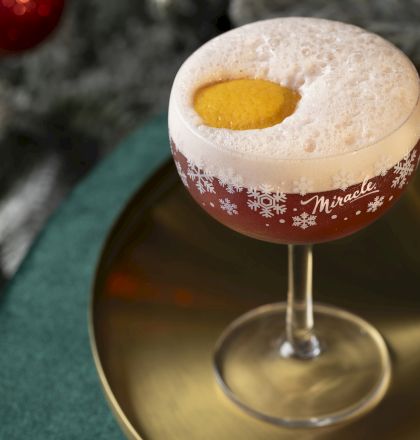 A festive cocktail in a frosted holiday glass with red-orange liquid and golden garnish, ready to sip for the season.