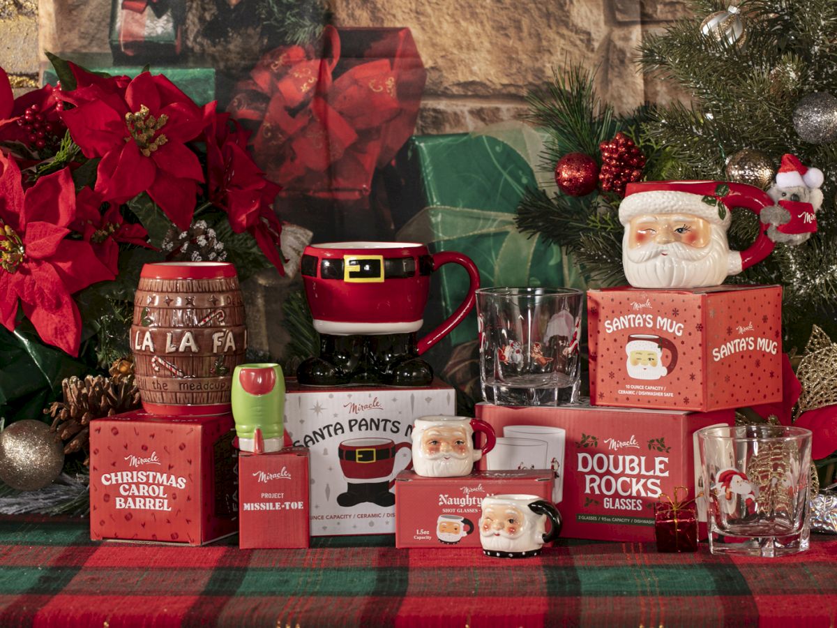 A festive holiday display with mugs, glassware, and boxes decorated for Christmas, surrounded by poinsettias and a Christmas tree.