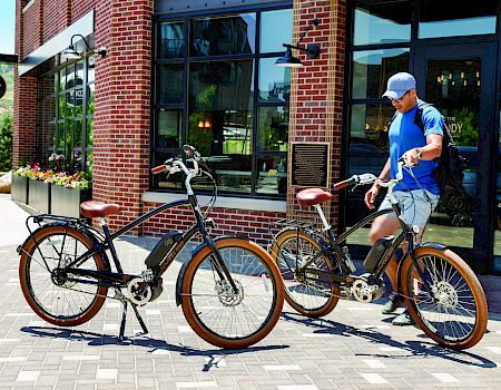 A person in blue attire adjusts two bicycles outside a brick building with a sign that reads "EDDY" in the background.