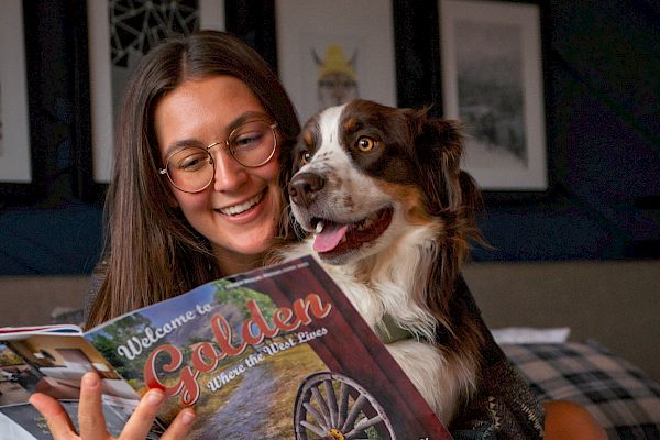 A person with glasses reads "Welcome to Golden" while holding a dog. A red mug labeled "The Eddy" is in the foreground.