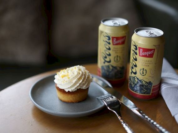 Two beer cans and a cupcake on a plate with a fork on a table, a casual snack setup.