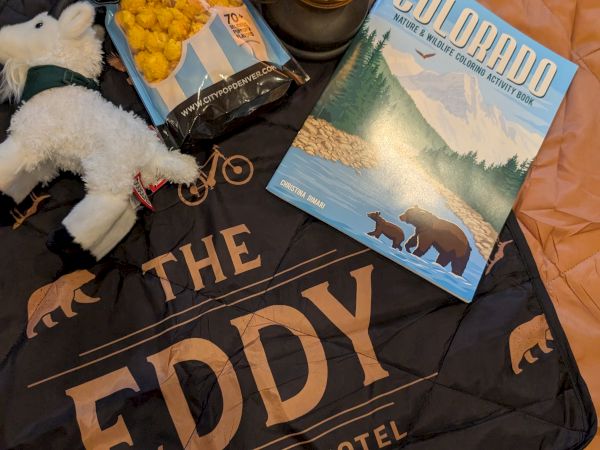 A cozy gift setup: a plush stuffed bear, warm lantern light, snack chips, and a &ldquo;Country&rdquo; wildlife coloring book.