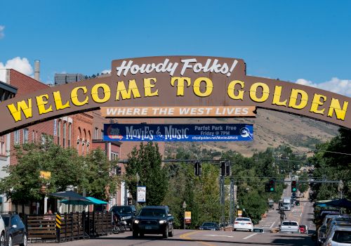 The image features a street scene with a large archway sign that reads "Howdy Folks! Welcome to Golden, Where the West Lives." Ending the sentence.