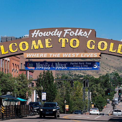 The image features a street scene with a large archway sign that reads "Howdy Folks! Welcome to Golden, Where the West Lives." Ending the sentence.