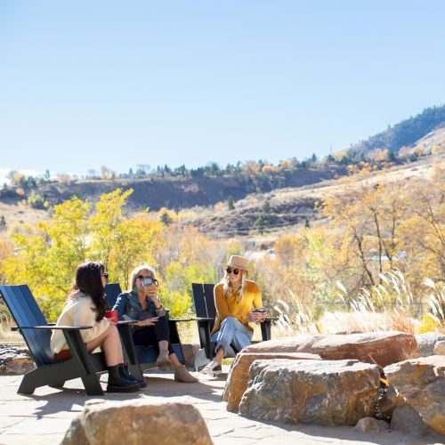 Three people sit in chairs on a sunny patio with a scenic mountainous backdrop.