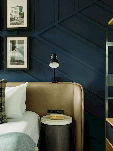 A stylish bedroom features framed photos, a plaid pillow, a nightstand with a lamp, and hanging robes on a wooden rack.