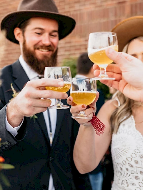 A group of people in hats are toasting with drinks, smiling in an outdoor setting.