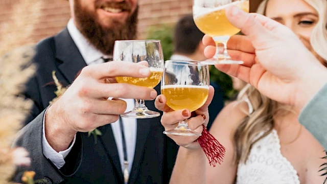 A group of people in hats are toasting with drinks, smiling in an outdoor setting.