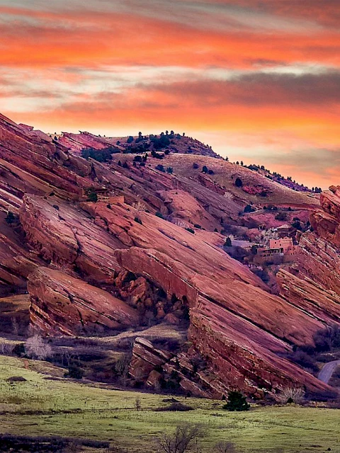 A stunning landscape featuring unique red rock formations under a vibrant sunset sky, with greenery and a winding road in the foreground.