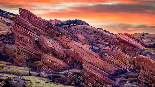 A stunning landscape featuring unique red rock formations under a vibrant sunset sky, with greenery and a winding road in the foreground.