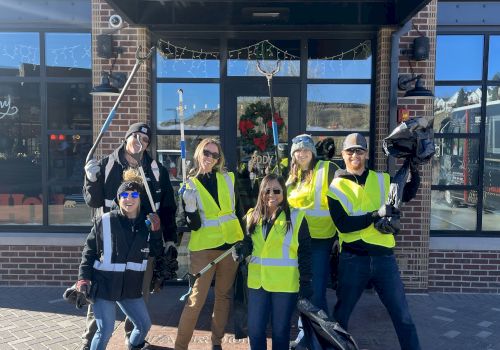 A group of people in yellow vests holding trash bags and pickers pose in front of a building with the number 1640.