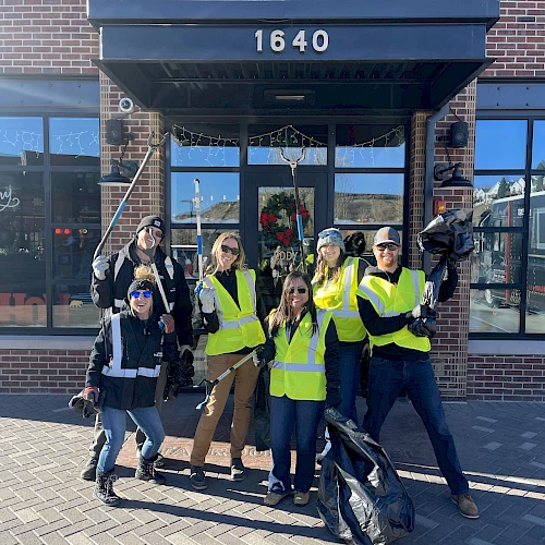 A group of people in yellow vests holding trash bags and pickers pose in front of a building with the number 1640.