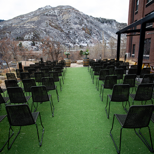 Rows of black chairs set up on artificial grass outdoors, with a mountainous backdrop.