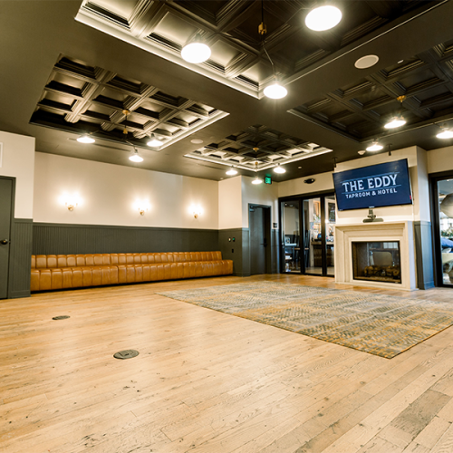 A spacious room with wooden floors, stylish ceiling, bench seating, a fireplace, and a sign reading "The Eddy" above the mantelpiece.