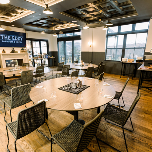 This image shows a cozy meeting room with round tables, chairs, and a fireplace at "The Eddy Taproom & Hotel."