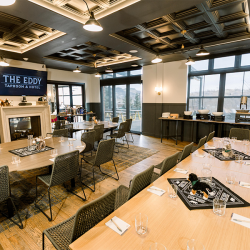 The image shows a restaurant dining area with a modern interior, featuring tables, chairs, large windows, and a sign reading "The Eddy".