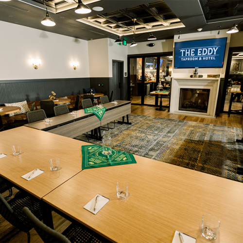 The image shows a conference room with tables set up in a U-shape facing a screen labeled "The Eddy Taproom & Hotel."