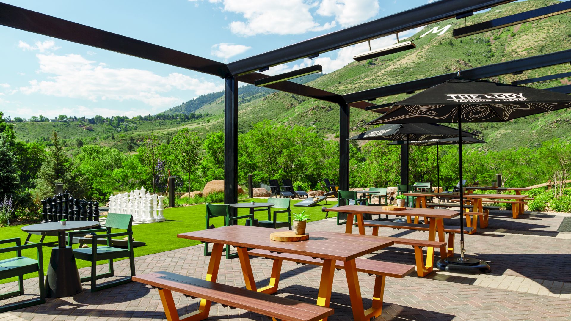 An outdoor patio with picnic tables, chairs, umbrellas, and a scenic view of green hills and clear skies, providing a peaceful dining atmosphere.