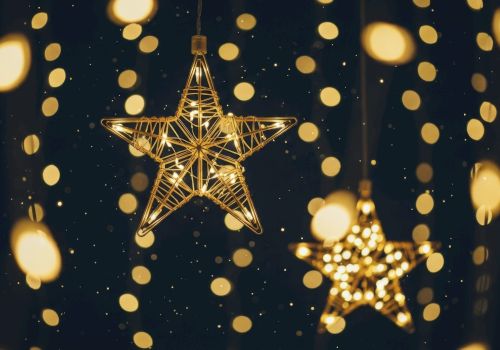 The image shows glowing star-shaped decorations hanging among blurred, circular lights on a dark background, creating a festive atmosphere.