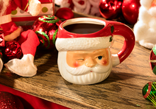 A festive scene with Santa-themed decorations, including a Santa mug, ornaments, candy canes, and figurines on a wooden surface.