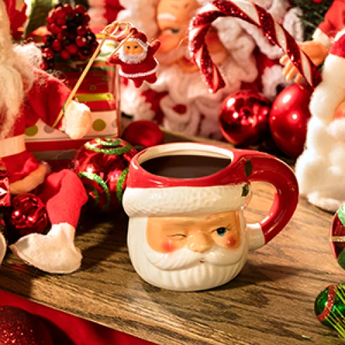 A festive scene with Santa-themed decorations, including a Santa mug, ornaments, candy canes, and figurines on a wooden surface.