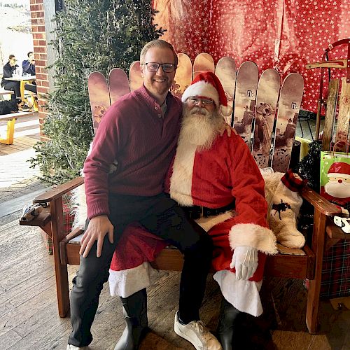 A person sits on Santa's lap in a festive setting with skis and red decorations in the background.