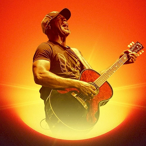 A guitarist wearing a cap plays an acoustic guitar against a dramatic orange-red sunset backdrop, glowing light radiating behind him.