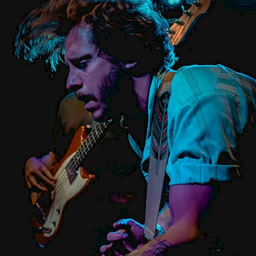 A musician playing an electric guitar on stage, blue lighting and a focused, energetic performance.