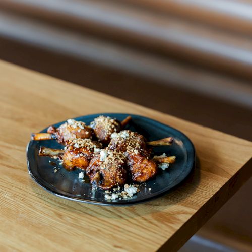 A plate of roasted chicken drumsticks sprinkled with herbs and crumbled cheese on a black dish.