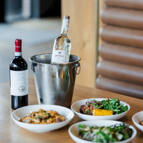 A table set with two wine bottles in an ice bucket and several dishes of pasta and salads, with wood beams in the background.