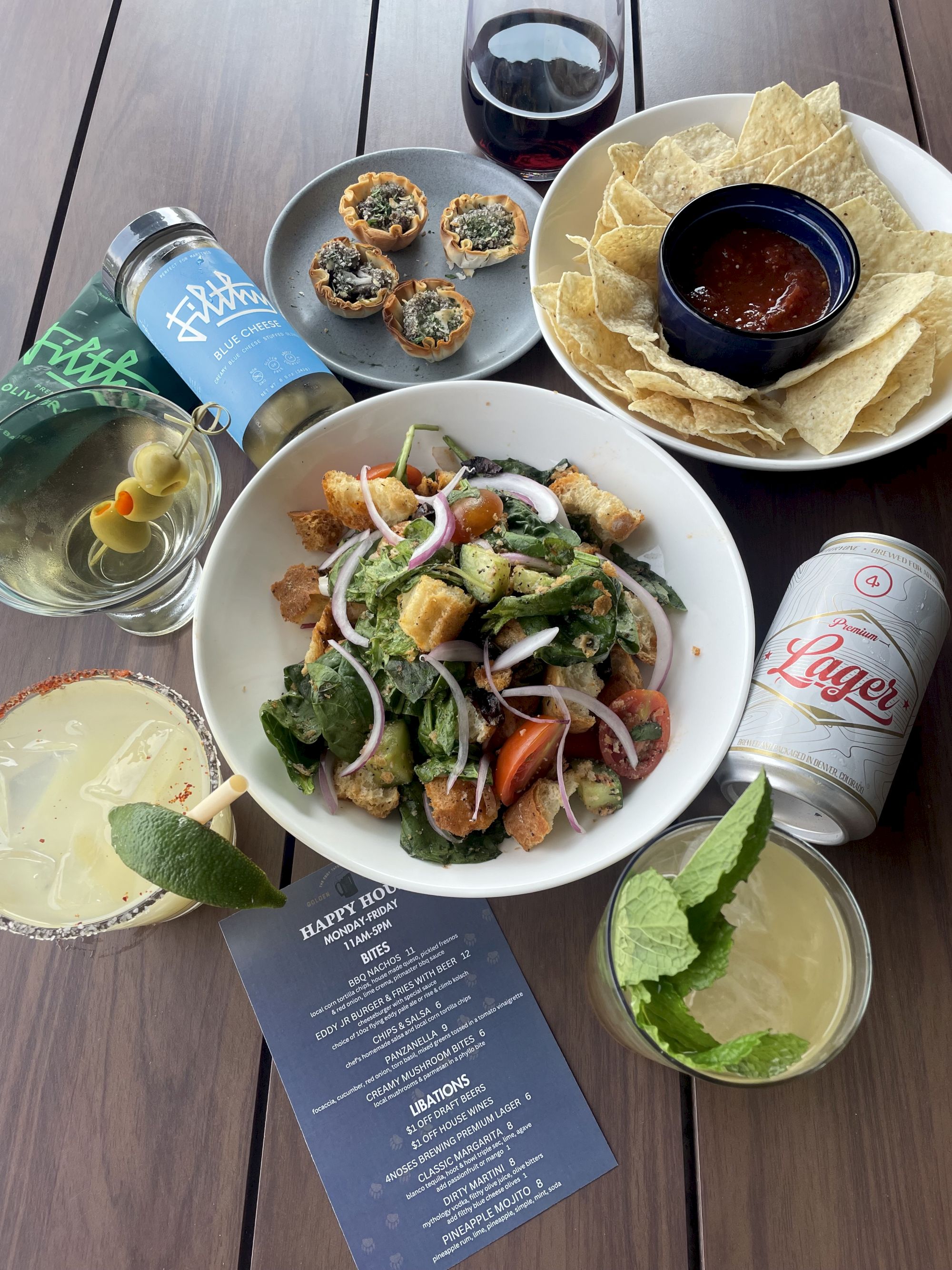 A table spread with Caesar salad, tortilla chips, cheesy bites, marinara, and drinks like Lagunitas beer, wine, and soda.