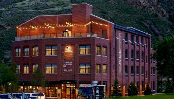 The image shows a four-story brick building with lights on the rooftop patio, labeled as a tavern & hotel, situated in a mountainous area.