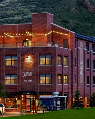 This image shows a multi-story brick building, likely a hotel, with lights strung across the rooftop and a truck parked out front in a grassy area.