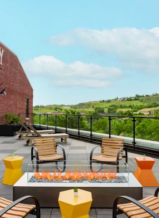 An outdoor seating area with a fire pit, colorful stools, and chairs. The sign reads "The Eddy Taproom & Hotel," with a scenic background.