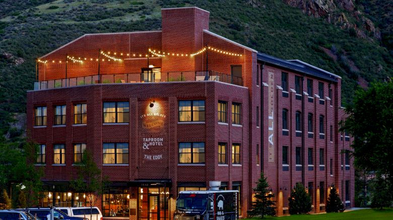 The image shows a brick building labeled "Ironbridge Tavern & Hotel" with string lights, 5th Street and surrounded by a mountainous landscape.