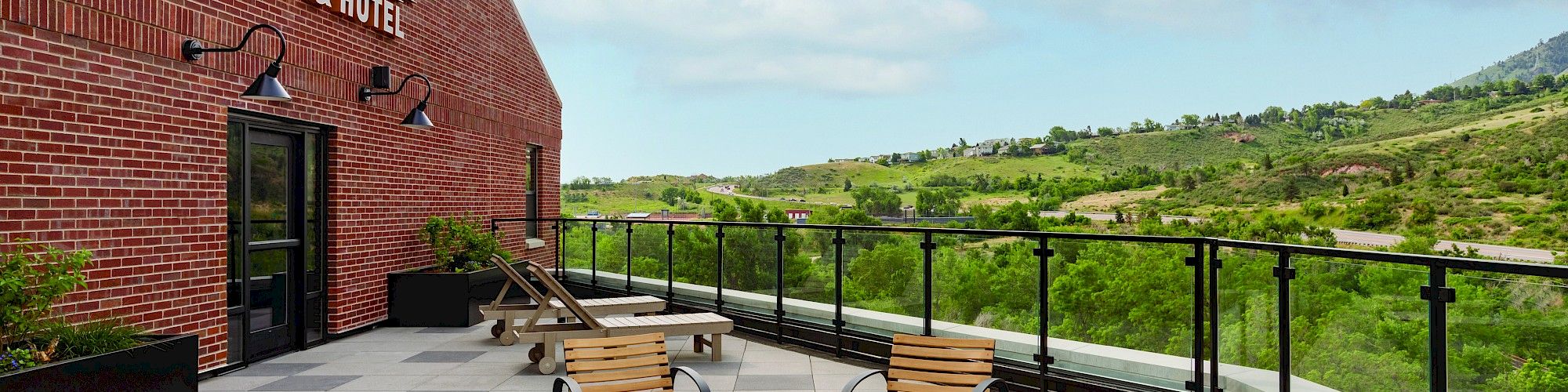 Outdoor seating area at The Eddy Taproom & Hotel featuring a fire pit, chairs, and tables, with a scenic view of the hills and greenery beyond the glass railing.